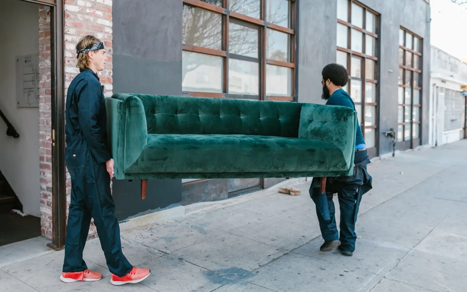 two junk removal workers carrying an old sofa out to the truck